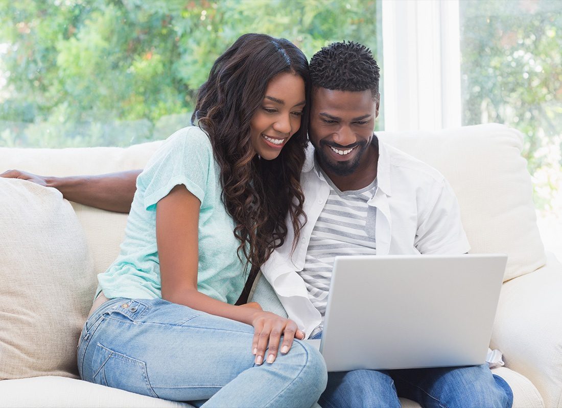 Read Our Reviews - Happy Couple on the Couch Using Their Laptop at Home
